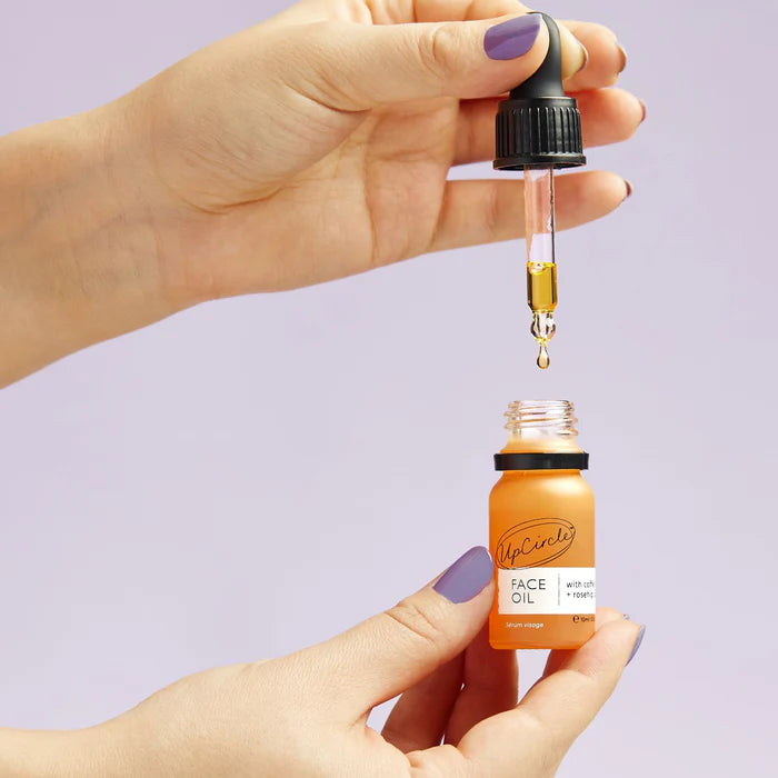 Hand holding a dropper with face oil over an orange bottle labeled 'McNulty's Face Oil' on a light purple background.